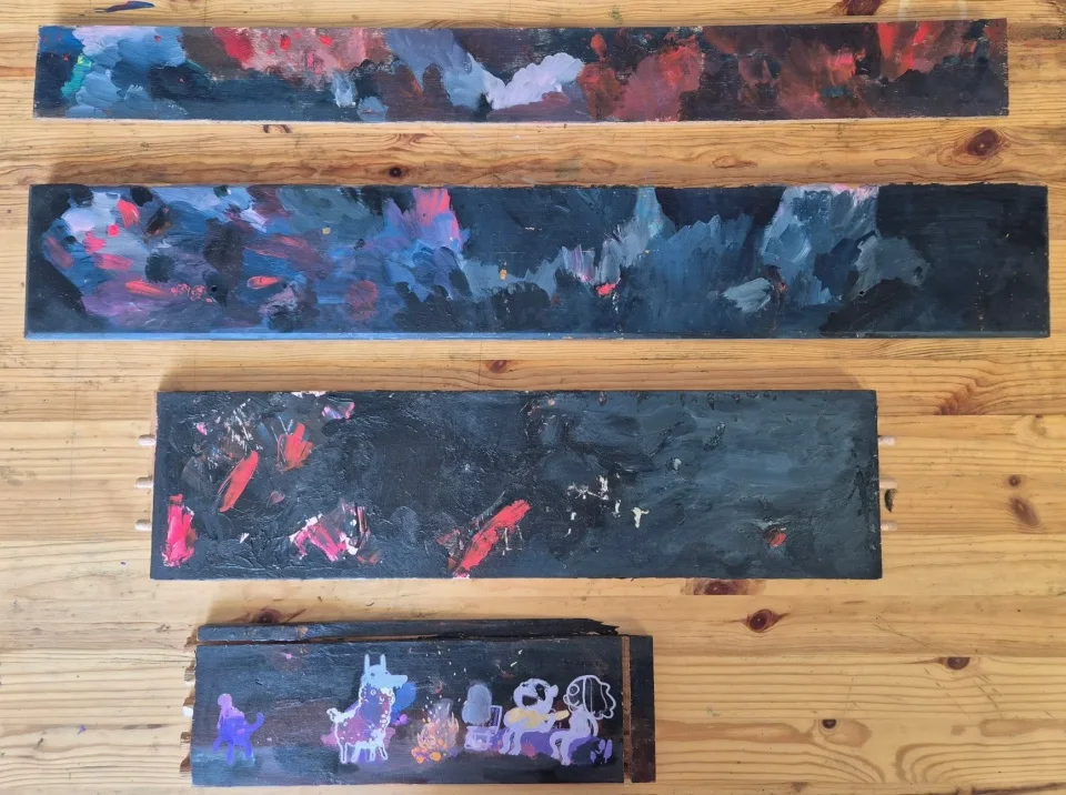 Four dark painted wood planks in red, blue and purple; the smallest shows a llama, a campfire and skull-faced figures.